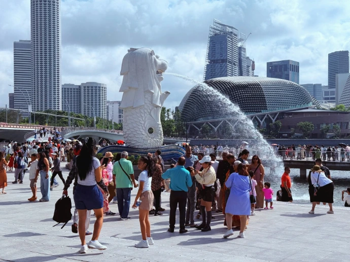 Crowds gather around the merlion statue with city skyline.